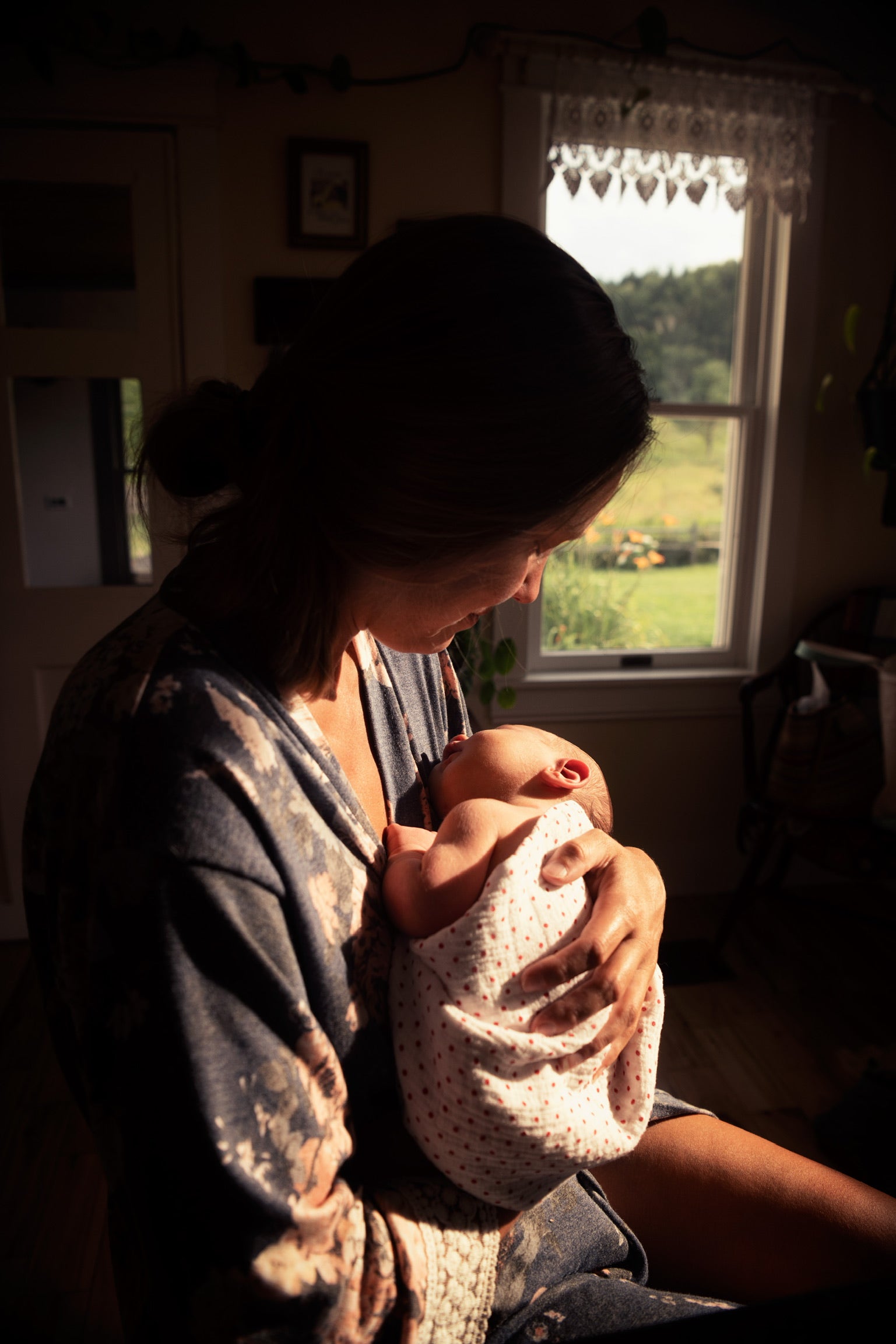 Woman breastfeeding a baby in a softly lit room with a window in the background.